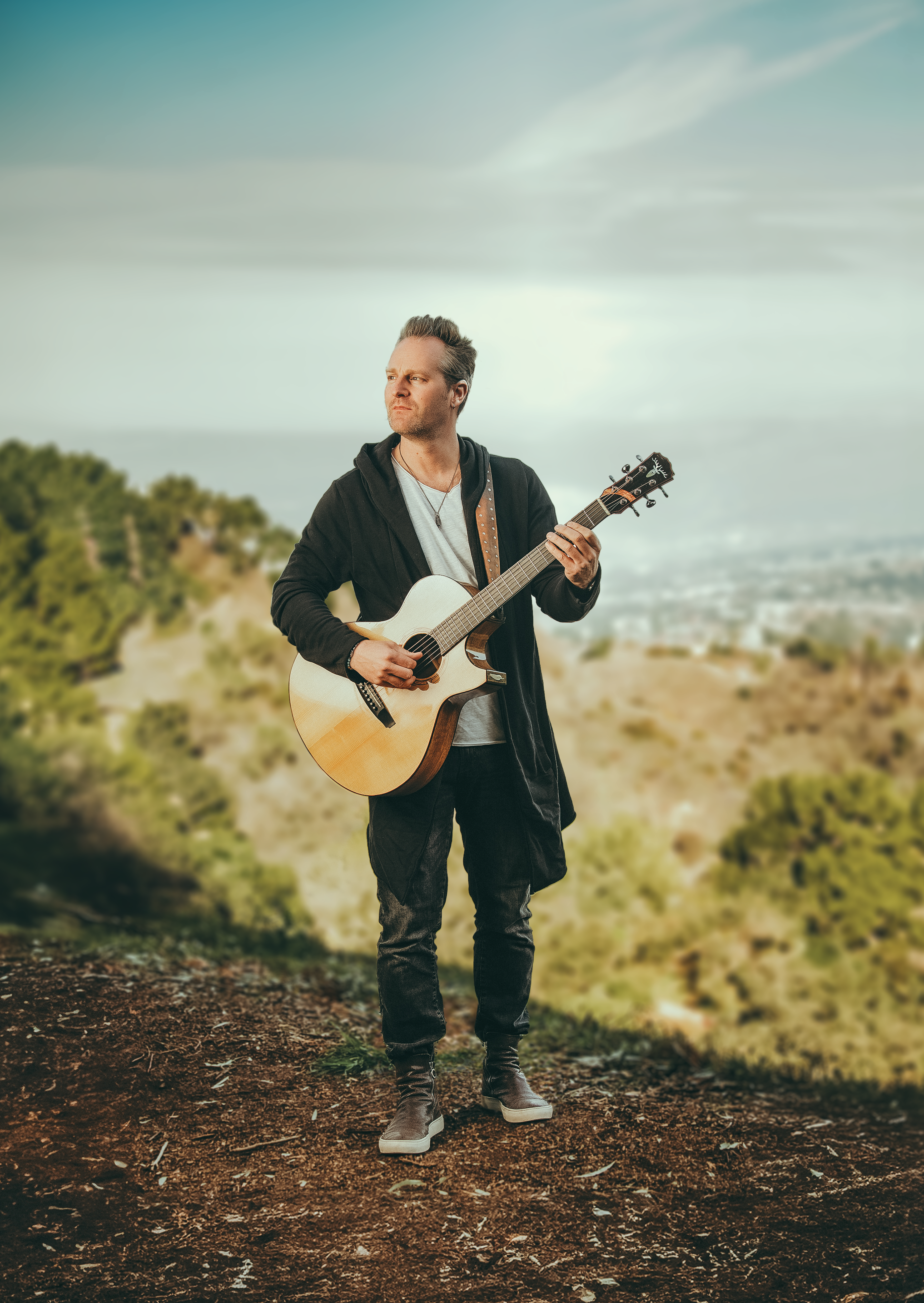 Man playing a guitar outdoors with a scenic background